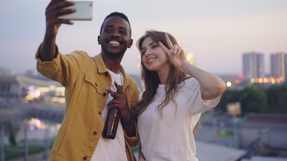 Attractive Multiracial Couple Is Taking Selfie with Smartphone at Rooftop Party, Man and Woman Are alt