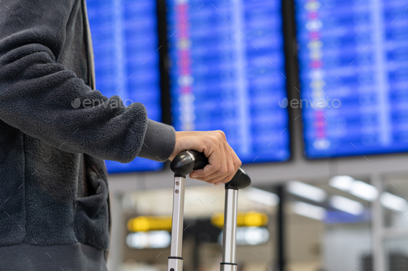 Young woman traveler with luggage looking at the flight information board in international airport Stock Photo by kitzstocker