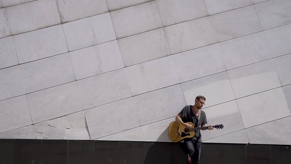 General Plan. Male Guitarist with the Glasses Leaned Back and Leg To the Great White Wall and Plays alt