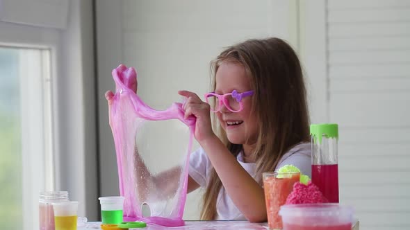 Little girl in glasses stretches a homemade pink slime and laughs