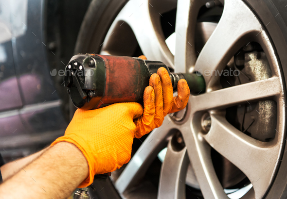 Mechanic unscrewing car wheel with impact wrench Stock Photo by Photology75