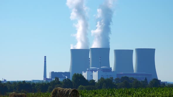 Factory (Nuclear Power Station) - Buildings and Smoke From Chimney - Field with Plants and Blue Sky alt