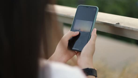 Close up young female scrolling pictures on a smartphone after taking a photo at the public park. alt