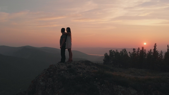 A Man and a Woman Stand on Top of the Mountain at Sunset