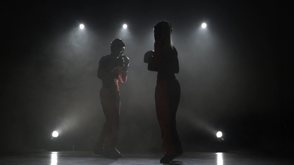 Guy with a Girl in Helmets and Boxing Gloves Beating in the Ring in the Dark Silhouette Light alt