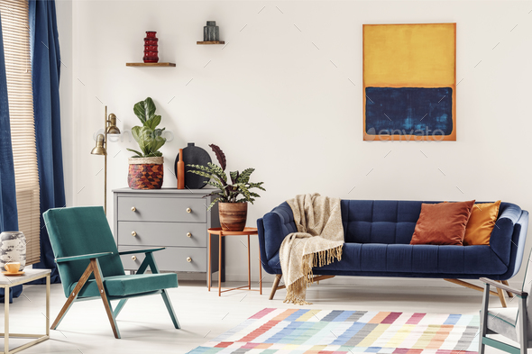 Orange end table with fresh plant standing next to navy couch wi Stock Photo by bialasiewicz