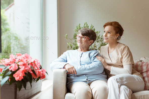 Geriatric woman and her professional caretaker sitting on a couc - Stock Photo - Images