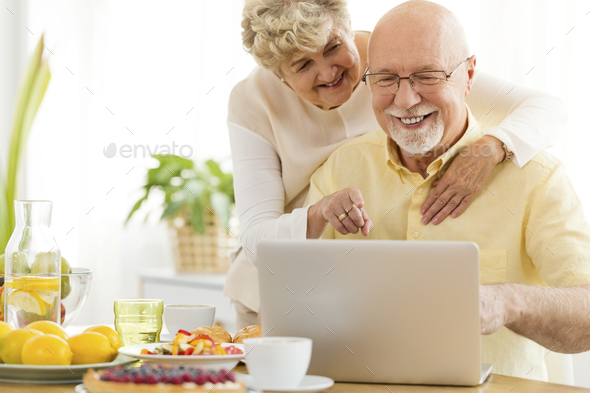 Smiling senior man using laptop with his happy wife. Elderly peo Stock Photo by bialasiewicz