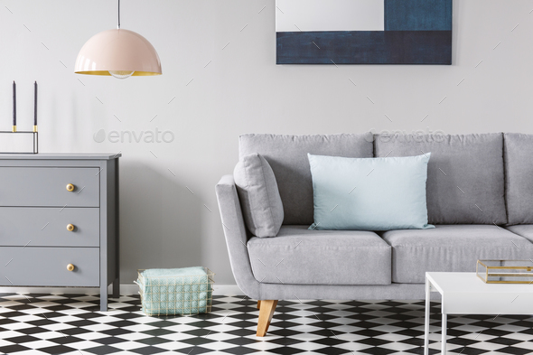 Pink lamp above grey cabinet next to sofa on checkered floor in Stock Photo by bialasiewicz
