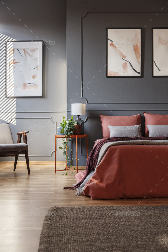 Orange bed against dark wall with molding and white posters next - Stock Photo - Images