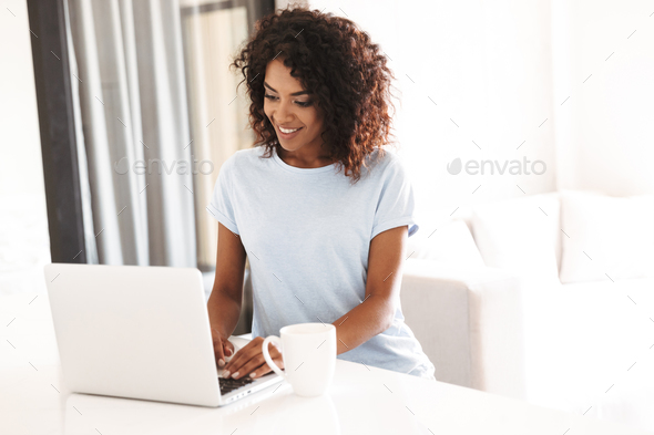Smiling african woman using laptop computer Stock Photo by vadymvdrobot