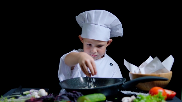 Little Boy Is Adding a Salt To the Dish, Wearing Chefs Suit and Cap alt