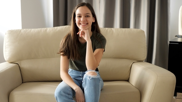Young Teenage Girl Is Sitting on the Couch and Smiles Naturaly To the Camera alt