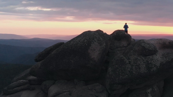 Drone Shot of Lonely Man Standing on Top of a Mountain and Enjoying the Sunset