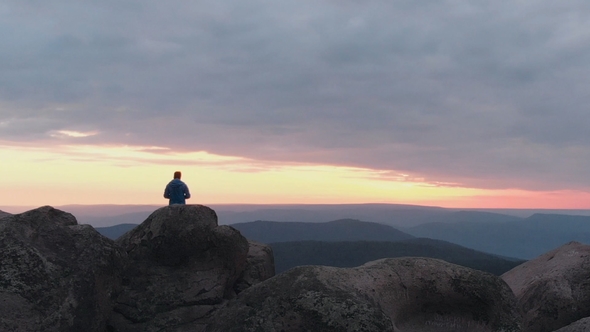 Drone Shot of Lonely Man Standing on Top of a Mountain and Enjoying the Sunset