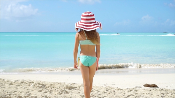 Adorable Little Girl in Big Hat Walking Along White Sand Beach