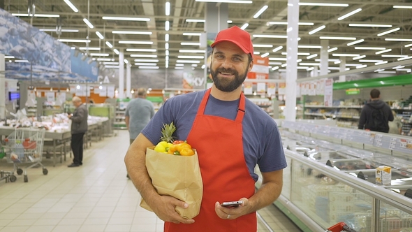 Handsome Delivery Man in Red Uniform with Paper Bag Standing in Supermarket