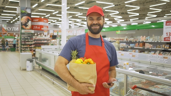 Handsome Delivery Man in Red Uniform with Paper Bag Standing in Supermarket