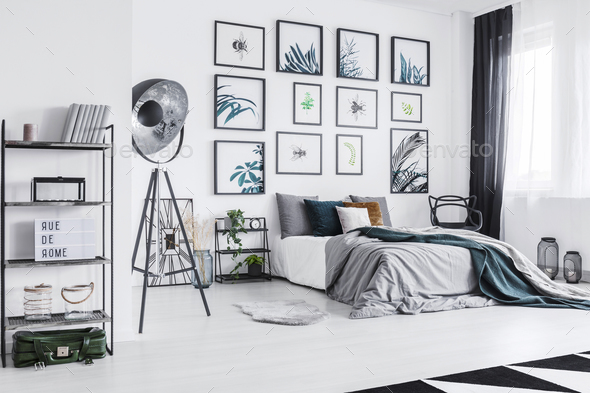 Real photo of a cozy bed standing next to a black lamp in a mono - Stock Photo - Images