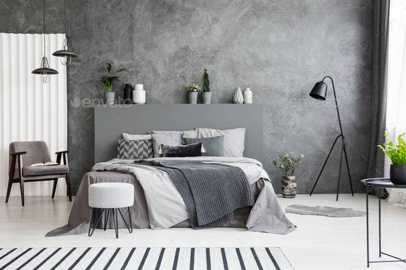 Grey armchair and stool near bed with headboard in bedroom inter Stock Photo by bialasiewicz