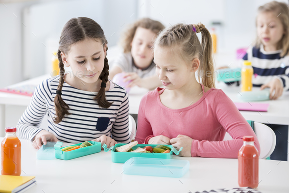 Two young girls during snack time in a school looking into each - Stock Photo - Images