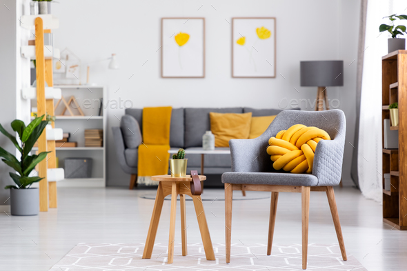 Yellow knot cushion on a gray armchair standing next to a wooden - Stock Photo - Images