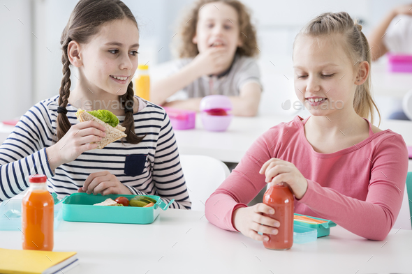 Front view of two junior girls in a school cafeteria during lunc Stock Photo by bialasiewicz