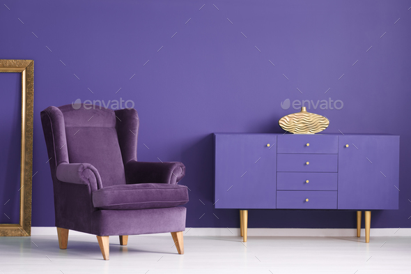 Purple cabinet with a golden vase, comfy armchair and frame in a Stock Photo by bialasiewicz