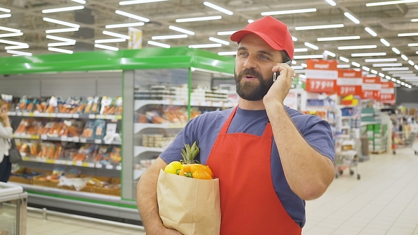 Handsome Delivery Man with Grocery Paper Bag Taking an Order Using a Smartphone in Supermarket