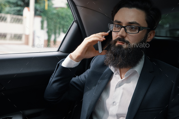 A businessman while traveling by car in the back seat using a sm - Stock Photo - Images