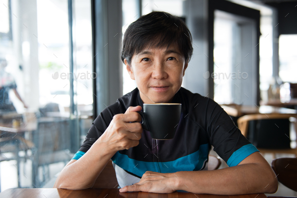 Senior Asian woman with coffee in cycling jersey Stock Photo by kenishirotie