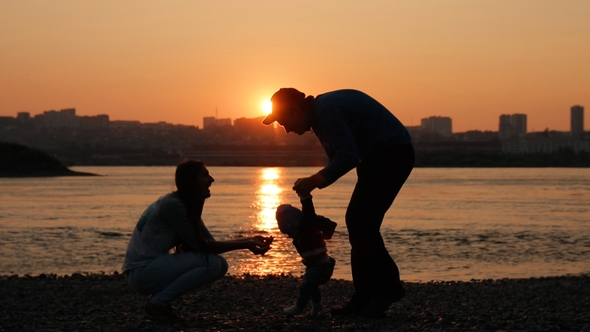 of a Young Family Walking By the River at Sunset