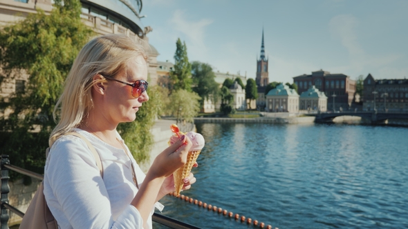 Woman Tourist Eating Ice Cream on the Background of the Recognizable View of Stockholm alt
