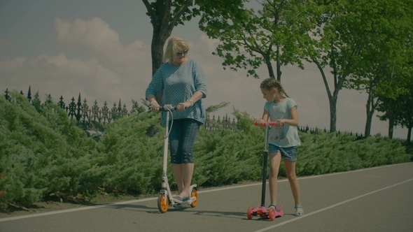 Grandmother and Granddaughter Riding Scooters in Park alt
