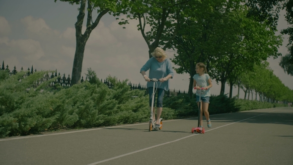 Grandchild Teaching Grandmom To Ride Scooter in Park alt