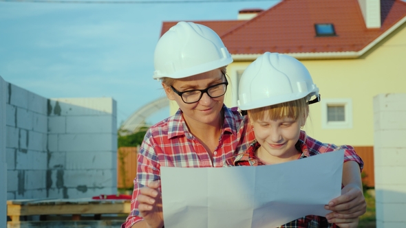 A Little Girl in a Helmet with a Young Mother Is Studying the Architectural Plan alt