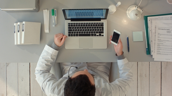 Doctor Having a Happy Conversation on Phone Mobile in His Office alt