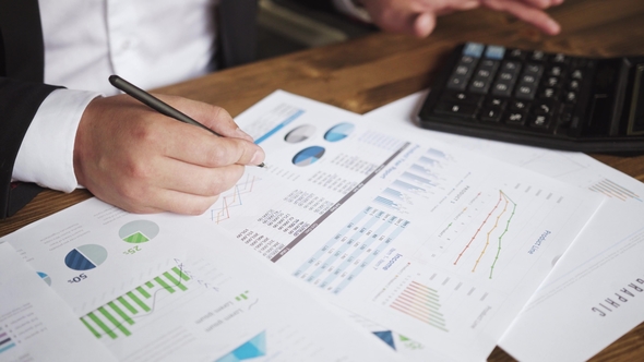 of a Businessman Hands with Pen Working at Office Desk and Analyzing Graphs and Charts and Writing alt