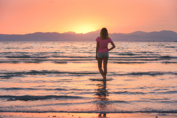 Young woman standing in sea with waves at sunset - Stock Photo - Images