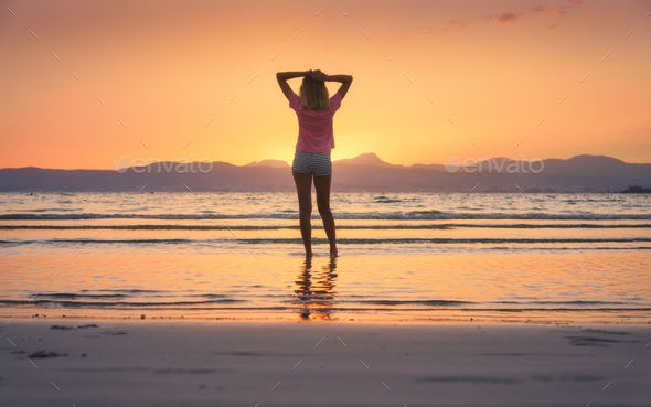 Young woman standing in sea with waves at sunset - Stock Photo - Images