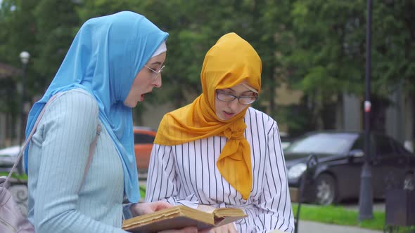 Two Muslim Women Students in Traditional Scarves with Books in Their Hands Communicate in the Park alt