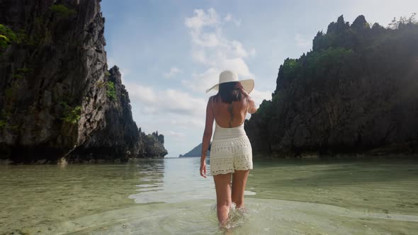 Woman In Sun Hat Walking In Sea On Hidden Beach alt