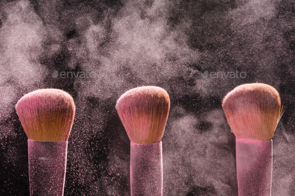 Three brushes for makeup with pink make-up mineral powder in motion on a black background Stock Photo by Satura_