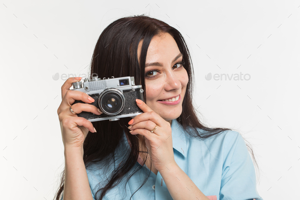 Photographer, hobby and people concept - Young brunette woman with retro camera on white background Stock Photo by Satura_