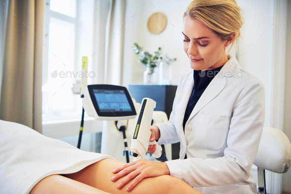 Clinic technician performing electrolysis on a female client's leg Stock Photo by UberImages