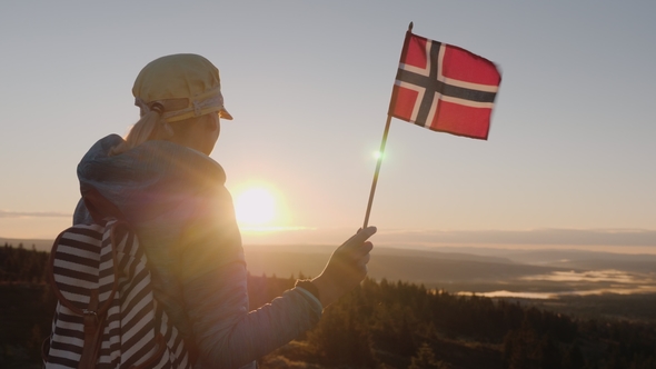 A Traveler with the Flag of Norway in His Hand Meets the Sunrise on the Top of the Mountain. Enjoys alt