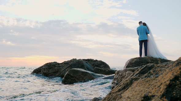 Beautiful Young Wedding Couple Standing on Sea Shore with Rocks. Newlyweds Spend Time Together alt
