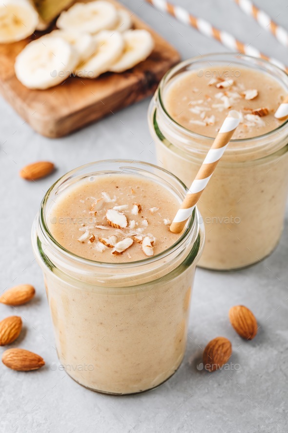 Banana almond smoothie with cinnamon and oat flakes and coconut milk in glass jars Stock Photo by nblxer