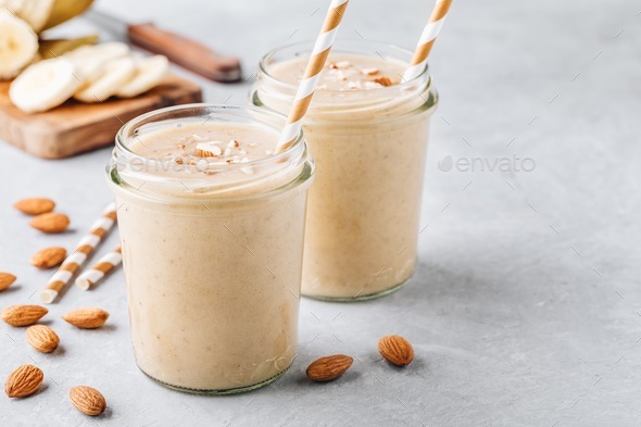 Banana almond smoothie with cinnamon and oat flakes and coconut milk in glass jars Stock Photo by nblxer