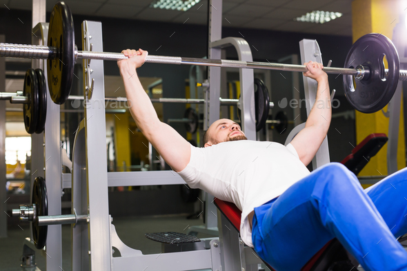 Sport, fitness, training and people concept - Man during bench press exercise in gym Stock Photo by Satura_